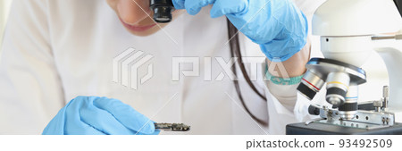 Woman scientist looking through magnifying glass at computer chip near microscope in laboratory 93492509