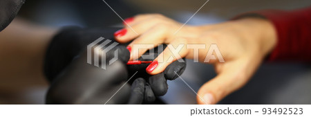 Manicurist painting woman nails with red varnish closeup Manicurist painting woman nails with red varnish closeup 93492523