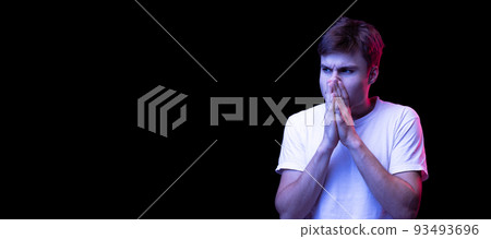Portrait of young man in white T-shirt posing isolated over black background in neon light. Shocked expression 93493696