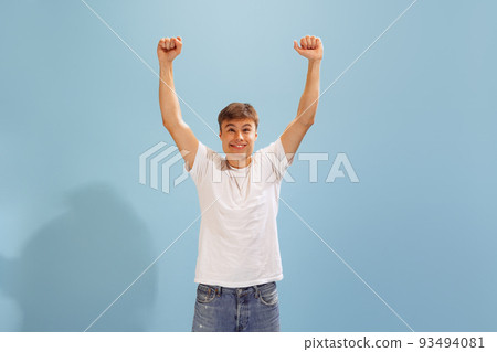 Portrait of young man posing, expressing cheerful, happy emotions isolated over blue studio background. Win Portrait of young man posing, expressing cheerful, happy emotions isolated over blue studio background. Win 93494081