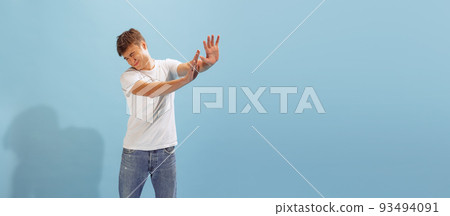Portrait of young man in casual T-shirt and jeans posing isolated over blue background. Stretching out hands to avoid something Portrait of young man in casual T-shirt and jeans posing isolated over blue background. Stretching out hands to avoid something 93494091