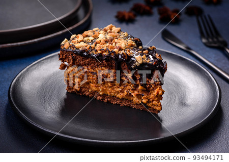 A piece of fresh delicious cake with nuts and chocolate on a black plate against a dark blue background A piece of fresh delicious cake with nuts and chocolate on a black plate against a dark blue background 93494171