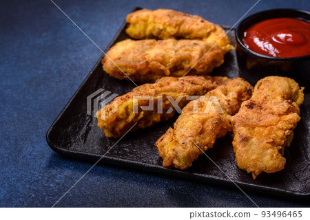 Fried crispy chicken nuggets with ketchup on black plate on a dark background 93496465