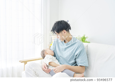 A baby taking a nap while being held by his father in the living room 93496577