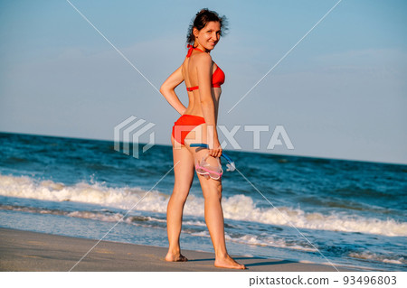 Sandy tanned woman with snorkeling equipment on the beach background. Happy lifestyle. Joyful woman in bikini standing along the beach to the sea. Sandy tanned woman with snorkeling equipment on the beach background. Happy lifestyle. Joyful woman in bikini standing along the beach to the sea. 93496803