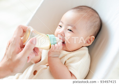 Smiling baby happily drinking milk 93497415