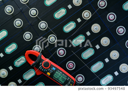 Electric vehicle lithium NMC battery with multimeter. Electric car battery manufacturing factory. Lithium-ion cell. Lithium NMC rechargeable battery. EV car energy storage. Automotive battery cell. 93497548
