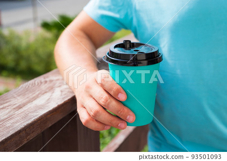 Emerald green color paper cup with black lid in Caucasian man's hand. Closeup, coffee cup, mockup. 93501093