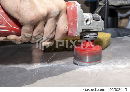 The tiler drills porcelain stoneware with a diamond crown. Close-up, selective focus. The tiler drills porcelain stoneware with a diamond crown. Close-up, selective focus. 93502445