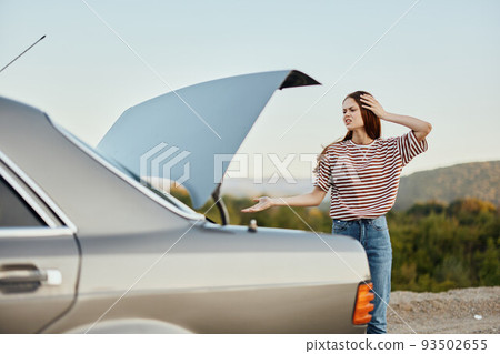 A woman sadly looks into the open trunk of a car during a stop on the road on the way to nature. 93502655