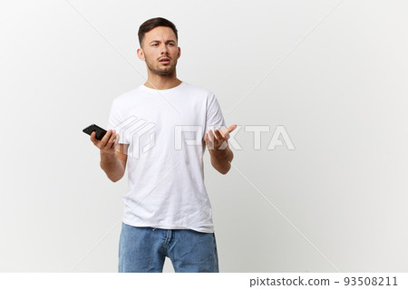 Confused unhappy tanned handsome man in basic t-shirt get shock info from phone message posing isolated on over white studio background. Copy space Banner Mockup. Distance online communication concept 93508211