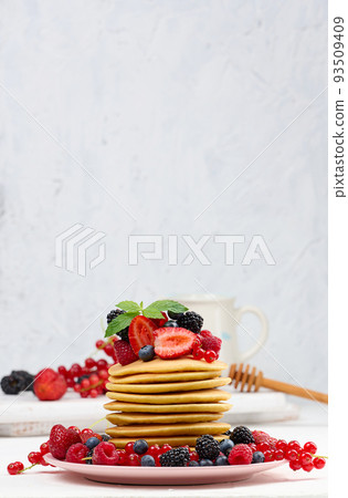 Stack of baked pancakes with fruits in a round plate on a white table, delicious breakfast Stack of baked pancakes with fruits in a round plate on a white table, delicious breakfast 93509409