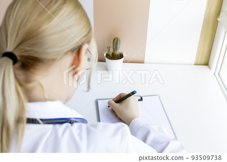 Close-up of a female doctor filling out a patient card on a clipboard during a consultation. 93509738