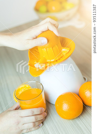 Awesome woman in the kitchen squeezing fresh orange juice with an electric juicer. 93511387