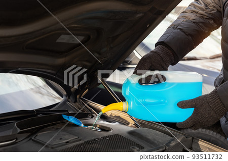 Close-up detail of driver or mechanic hand in gloves pouring blue antifreeze liquid for winter car windshield screen washing with bootle watering can. Car seasonal service and maintenance concept 93511732
