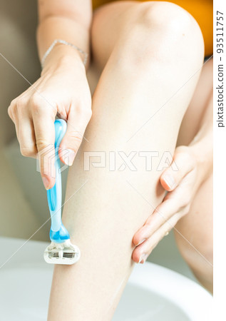 Close up of hand woman shaves leg disposable razor. Moistening and hair removal concept. 93511757
