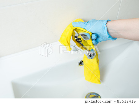 Female hands with blue rubber protective gloves cleaning tap with yellow cloth. Concept Spring cleaning Female hands with blue rubber protective gloves cleaning tap with yellow cloth. Concept Spring cleaning 93512419