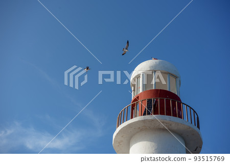 Top of a white-red lighthouse against a blue sky with an airplane. Top of a white-red lighthouse against a blue sky with an airplane. 93515769
