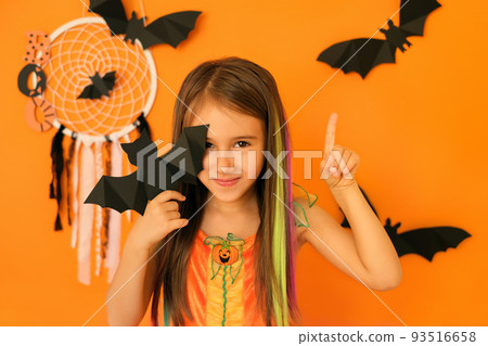 Child shows something above her head gesturing, pointing with index finger upwards, isolated over orange background in studio with halloween decor. nice and attractive cute girl Child shows something above her head gesturing, pointing with index finger upwards, isolated over orange background in studio with halloween decor. nice and attractive cute girl 93516658