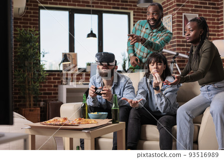 Diverse group of friends having fun with vr glasses and video games, playing competition with augmented reality goggles. People feeling happy together at party gathering with alcohol. 93516989