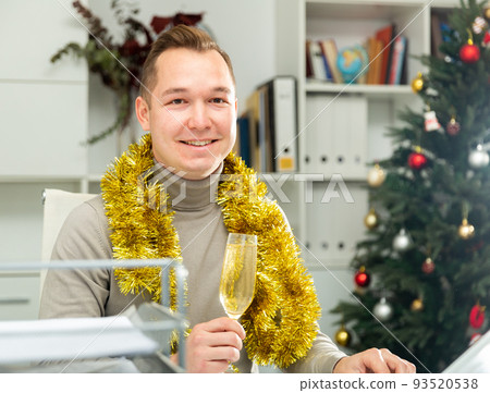 Cheerful man office worker sitting at table in Christmas decorated office Cheerful man office worker sitting at table in Christmas decorated office 93520538