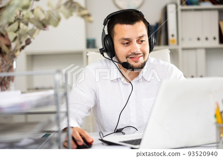Smiling man with headset in his workplace in office Smiling man with headset in his workplace in office 93520940