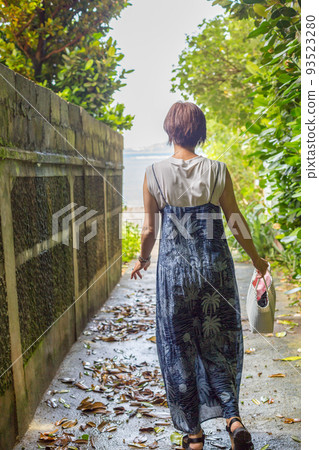 Okinawa's power spot "Fukugi Namiki", a traveling girl walking on a sandy road lined with hundreds of years old Fukugi trees 93523280
