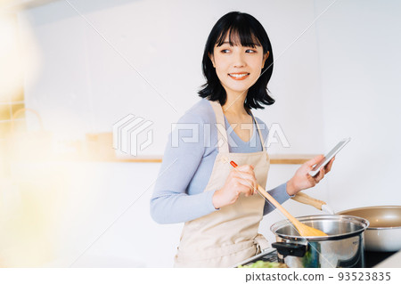 A woman cooking while watching a smartphone 93523835