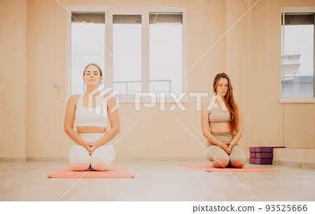 Two young sporty woman, fitness instructor in sportswear doing stretching and pilates on yoga mat in the studio with mirror. Female fitness yoga routine concept. Healthy lifestyle and harmony. Two young sporty woman, fitness instructor in sportswear doing stretching and pilates on yoga mat in the studio with mirror. Female fitness yoga routine concept. Healthy lifestyle and harmony. 93525666