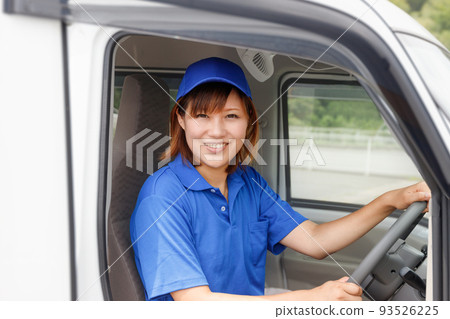 一個戴著藍色帽子和馬球衫的女人開車。移動的送貨司機的圖像。 一個戴著藍色帽子和馬球衫的女人開車。移動的送貨司機的圖像。 93526225
