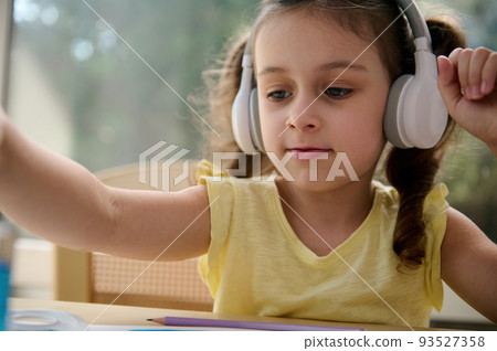 Close-up portrait of European child girl of preschool, listening to the music in wireless headphones, holding a paintbrush and painting picture with watercolors in a creative art class. Kids hobby Close-up portrait of European child girl of preschool, listening to the music in wireless headphones, holding a paintbrush and painting picture with watercolors in a creative art class. Kids hobby 93527358