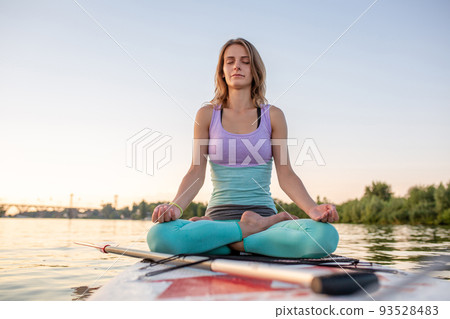 Young beautiful woman meditating in a sea at SUP paddleboarding. Healthy lifestyle. 93528483