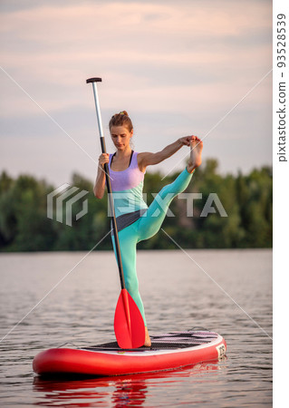 Sporty woman in yoga position on paddleboard, doing yoga on sup board, exercise for flexibility and stretching of muscles Sporty woman in yoga position on paddleboard, doing yoga on sup board, exercise for flexibility and stretching of muscles 93528539