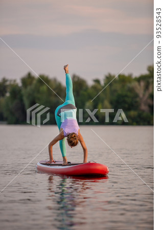 Sporty woman in yoga position on paddleboard, doing yoga on sup board, exercise for flexibility and stretching of muscles Sporty woman in yoga position on paddleboard, doing yoga on sup board, exercise for flexibility and stretching of muscles 93528543