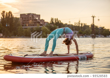 Sporty woman in yoga position on paddleboard, doing yoga on sup board, exercise for flexibility and stretching of muscles Sporty woman in yoga position on paddleboard, doing yoga on sup board, exercise for flexibility and stretching of muscles 93528583