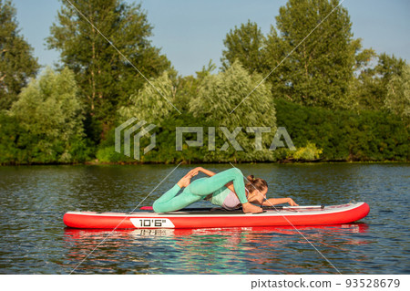 Woman practicing yoga on the paddle board in the morning 93528679