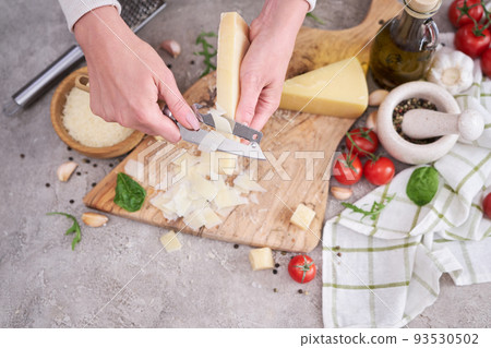Woman slicing Parmesan cheese on a wooden cutting board at domestic kitchen 93530502