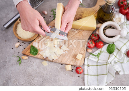 Woman slicing Parmesan cheese on a wooden cutting board at domestic kitchen Woman slicing Parmesan cheese on a wooden cutting board at domestic kitchen 93530505