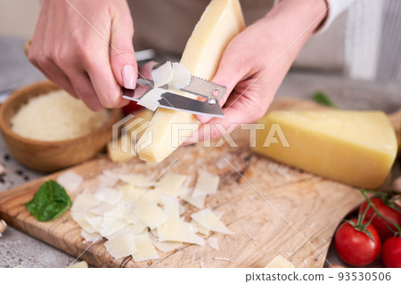 Woman slicing Parmesan cheese on a wooden cutting board at domestic kitchen 93530506