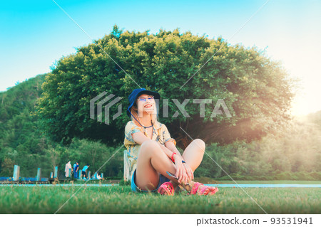 Woman is sitting beside a large tree in a park for, nature and freedom concept.. Woman is sitting beside a large tree in a park for, nature and freedom concept.. 93531941
