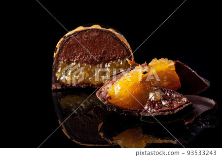 Cut luxury handmade candy with chocolate and yellow confiture filling on black background. 93533243