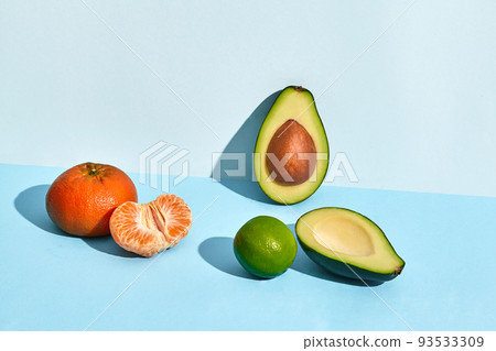 Composition of fresh fruits, mandarin lime and two halfs of cutted avocado on two-colored background 93533309