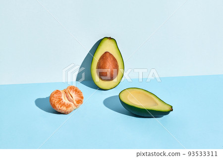 Composition of fresh fruits, mandarin and two halfs of cutted avocado on two-colored background Composition of fresh fruits, mandarin and two halfs of cutted avocado on two-colored background 93533311