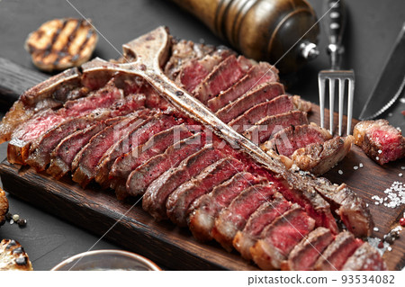 Sliced Steak T-bone lying on wooden board. Grilled vegetables in a pan grill. Black background. Close-up 93534082