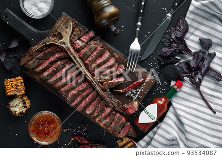 Sliced Steak T-bone lying on wooden board. Grilled vegetables in a pan grill. Black table with gray cloth 93534087