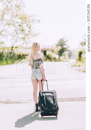 Beautiful young blonde girl smiling on the sunny road with suitcase luggage . Traveling the world with hitchhiking. Beautiful young blonde girl smiling on the sunny road with suitcase luggage . Traveling the world with hitchhiking. 93534536