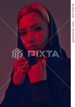 Young pretty woman wearing a black hood and shorts on dark background. Portrait Young pretty woman wearing a black hood and shorts on dark background. Portrait 93535676