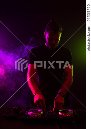 Attractive young DJ playing on turntables with color light effects 93535720