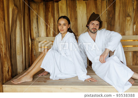 Portrait of young man and woman sitting on wooden bench in sauna Portrait of young man and woman sitting on wooden bench in sauna 93538388