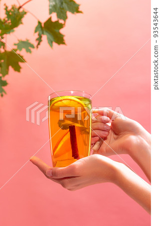 Glass of delicious citrus tea with lemons mint and cinnamon stick isolated over pink background. Vitamin drink Glass of delicious citrus tea with lemons mint and cinnamon stick isolated over pink background. Vitamin drink 93543644